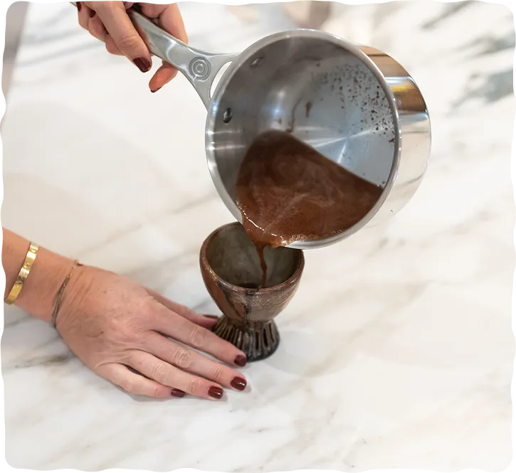 Pouring warm ceremonial cacao from a pan into a cup